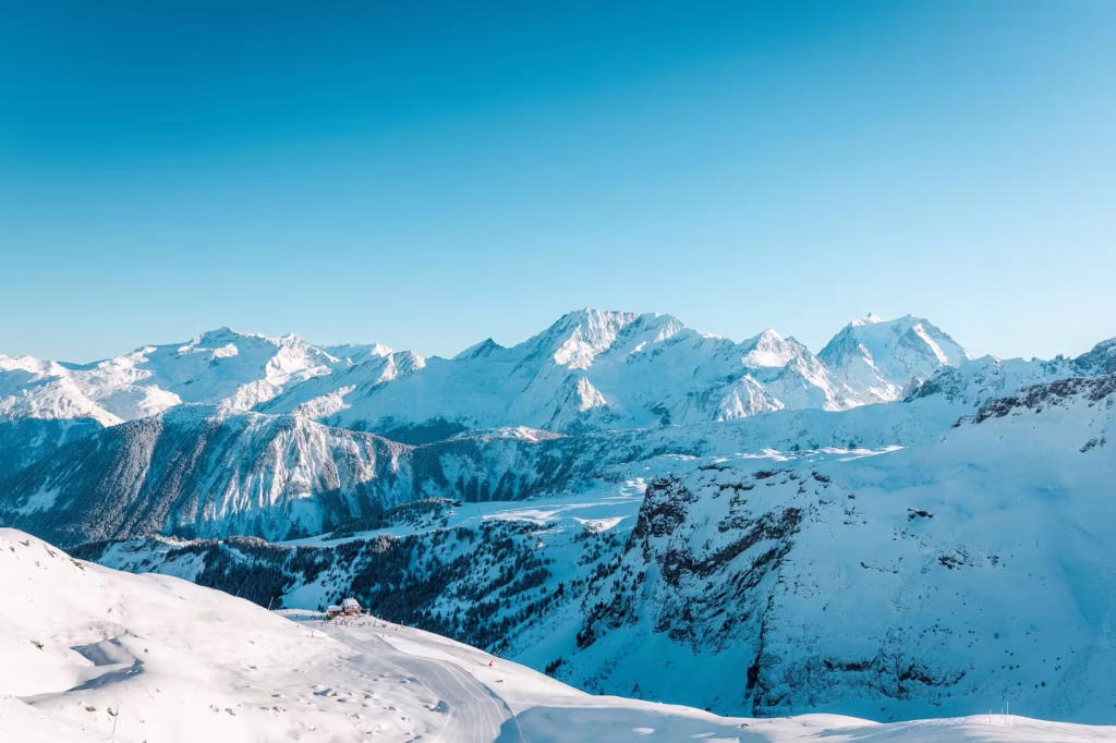 Vue aerienne sur une piste de ski menant a un refuge de montagne, chaine de sommets enneiges.