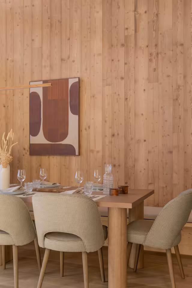 Salle a manger habillee de bois, tables dressees avec verres a vin, oeuvre d'art murale.