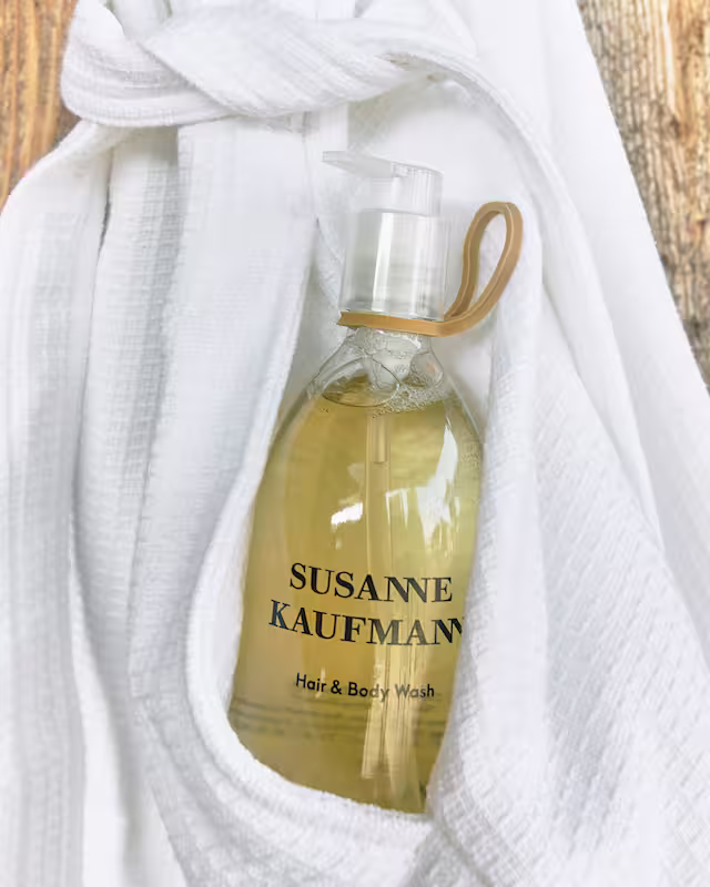 Flacon de gel douche et cheveux Susanne Kaufmann glisse dans les plis d'un peignoir blanc.